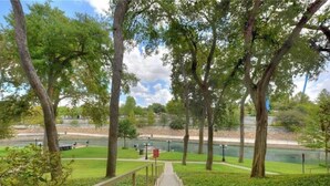 A pathway leading to a park with trees and a body of water in the background.