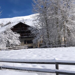 Eine Holzhütte mit einem Balkon, umgeben von schneebedeckten Bäumen und wolkenlosem, blauem Himmel.