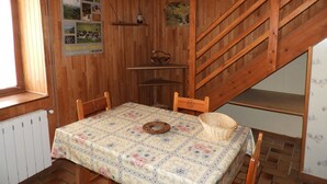 Una habitació de fusta amb una taula coberta amb un mantell floral, una cadira de fusta, una petita estant i una escala de fusta.
