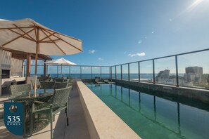 Et tag med uendeligt pool, glasgelændere, udendørs siddepladser og udsigt over havet og byens skyline.
