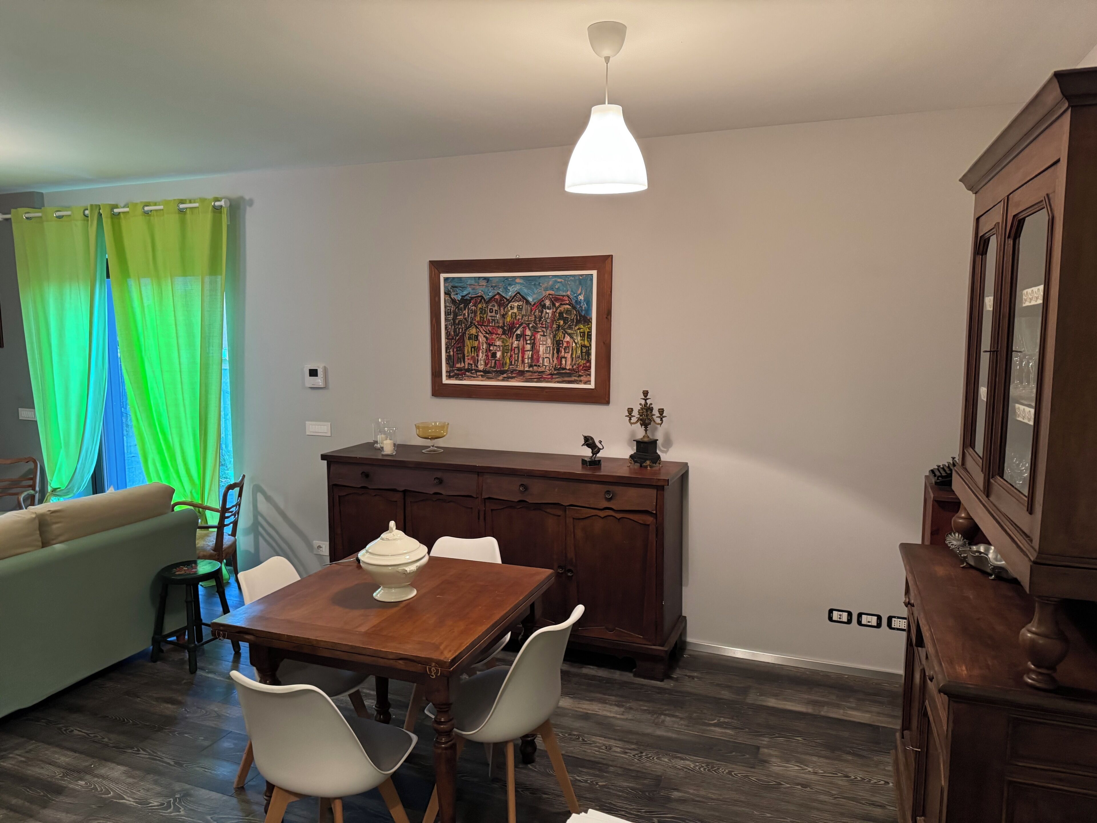 A dining area with a wooden table, two chairs, a painting on the wall, and a cabinet.