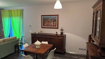 A dining area with a wooden table, two chairs, a painting on the wall, and a cabinet.