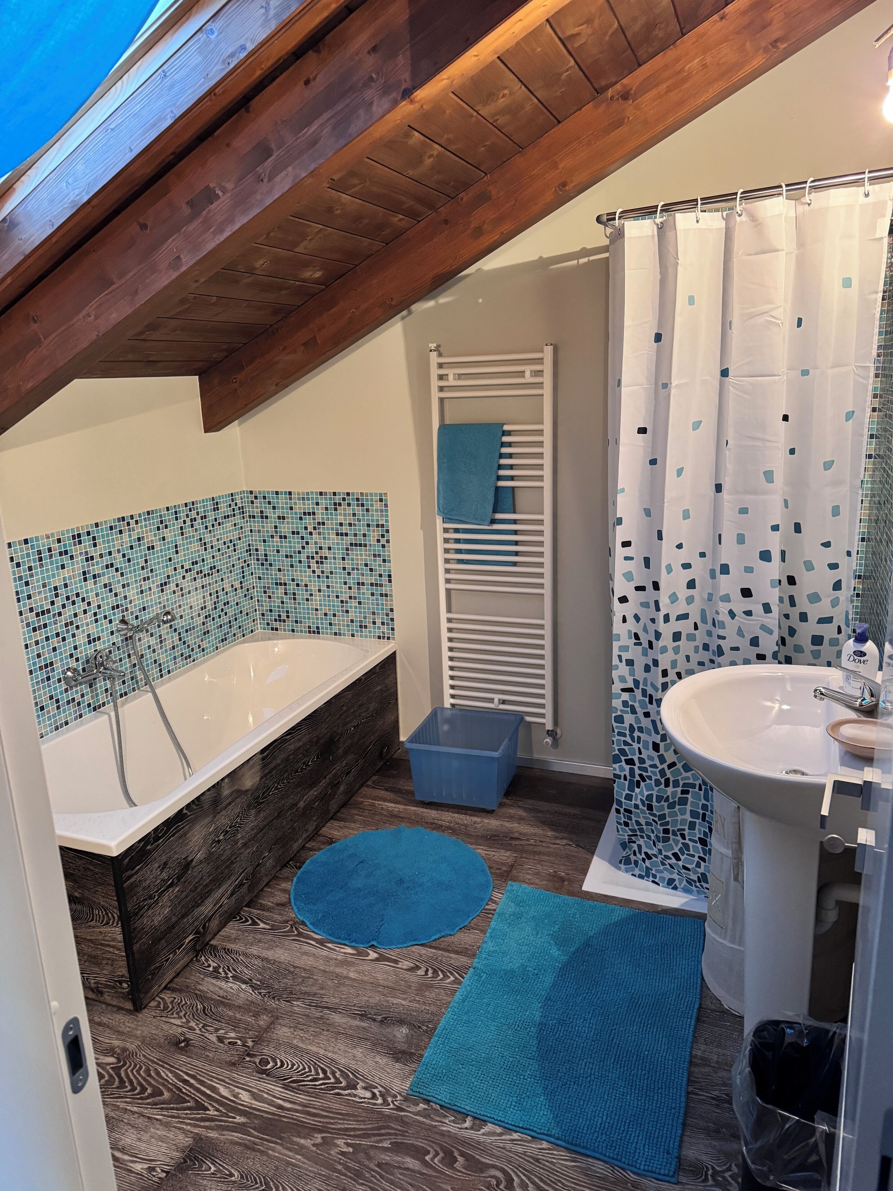 Une salle de bain avec une baignoire en bois, un lavabo blanc, un rideau de douche à motifs bleus et un mur carrelé.