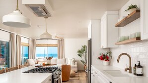 Une cuisine moderne dotée d’un îlot central, de meubles blancs et offrant une vue sur l’extérieur.