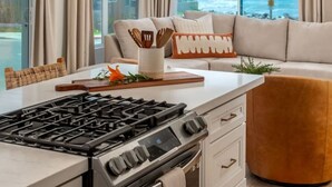 Une cuisine moderne équipée d’une cuisinière à gaz, un coin repas avec une table blanche et une grande fenêtre donnant sur l’océan.