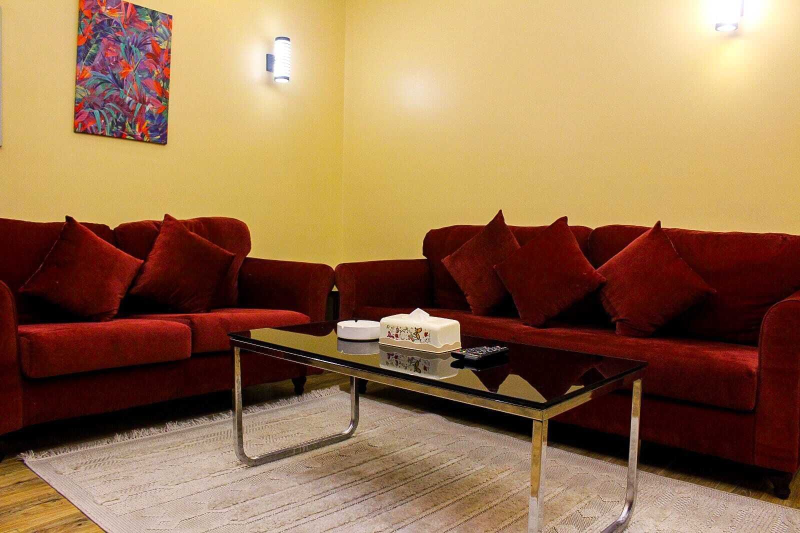Un salon avec deux canapés rouges, une table basse en verre et une boîte à mouchoirs blanche.