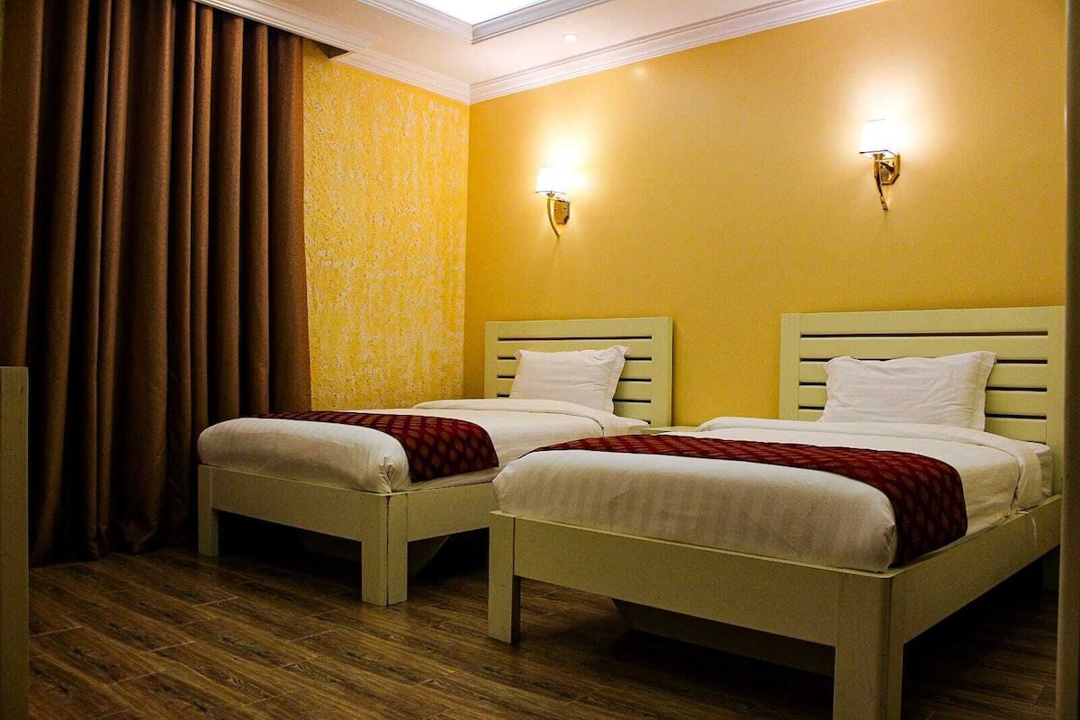A hotel room with two single beds, wooden flooring, and yellow walls.