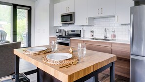 Une cuisine moderne avec des meubles blancs, des appareils en acier inoxydable et une table à manger en bois, mise avec des assiettes et des verres.