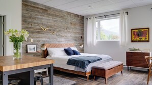 Une chambre à coucher avec une tête de lit en bois, un lit avec une literie blanche et bleue, une table de chevet en bois, un bureau et une fenêtre avec des rideaux.