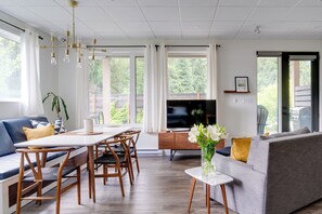 Una sala de estar moderna con comedor, un sofá, un televisor y una planta.