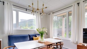 Une pièce moderne avec une table blanche, un canapé bleu et une grande fenêtre donnant sur un paysage verdoyant.