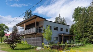 Une maison moderne à deux étages, dotée d’un balcon, entourée d’un jardin bien entretenu et d’arbres.