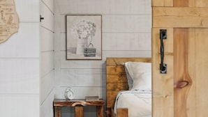 Een slaapkamer met een houten hoofdbord, een nachtkastje met een klok en boeken, en een lijst met een foto aan de muur.