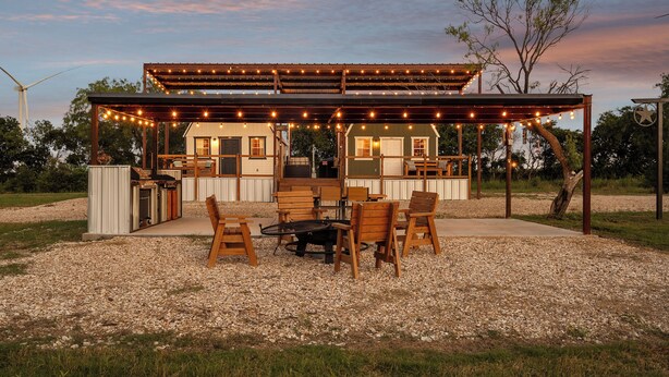 A covered outdoor patio with string lights, a grill, and wooden furniture.