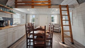 A kitchen with wooden cabinets, a dining table, and chairs. There is a wooden ladder leaning against the wall.