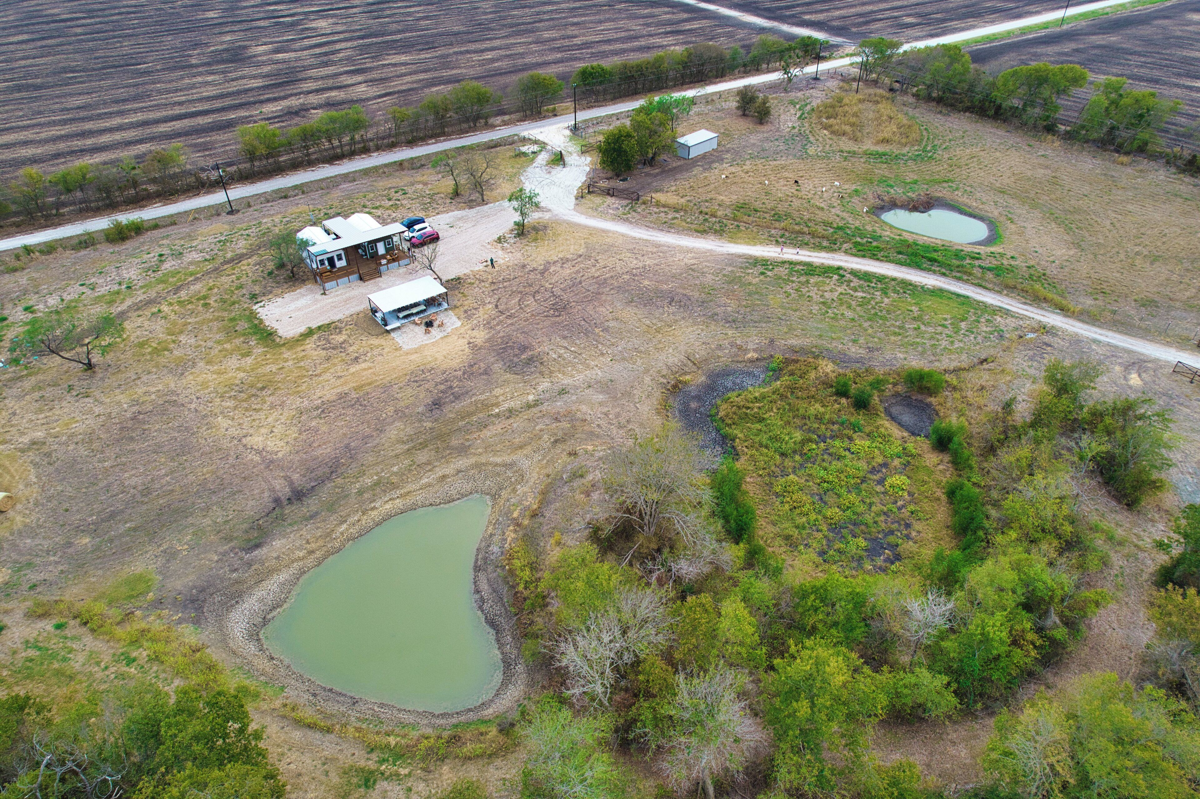 Vue aérienne d’une propriété rurale avec une maison, un petit étang et un chemin de terre.