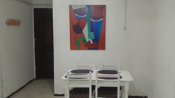 Una habitación con una pared blanca, una puerta y un cuadro. Hay dos sillas blancas con cojines morados.