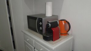 Una kitchenette con microondas, cafetera y un rollo de toallas de papel sobre una encimera blanca.