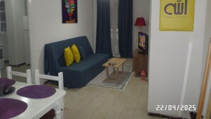Una sala de estar con un sofá azul, una mesita, un televisor y un letrero amarillo en la pared.