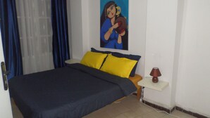 Un dormitorio con una cama, dos almohadas amarillas, una mesita de noche con lámpara y un cuadro en la pared.
