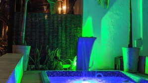 Piscina com cachoeira, cercada por palmeiras e uma estrutura de pérgola.