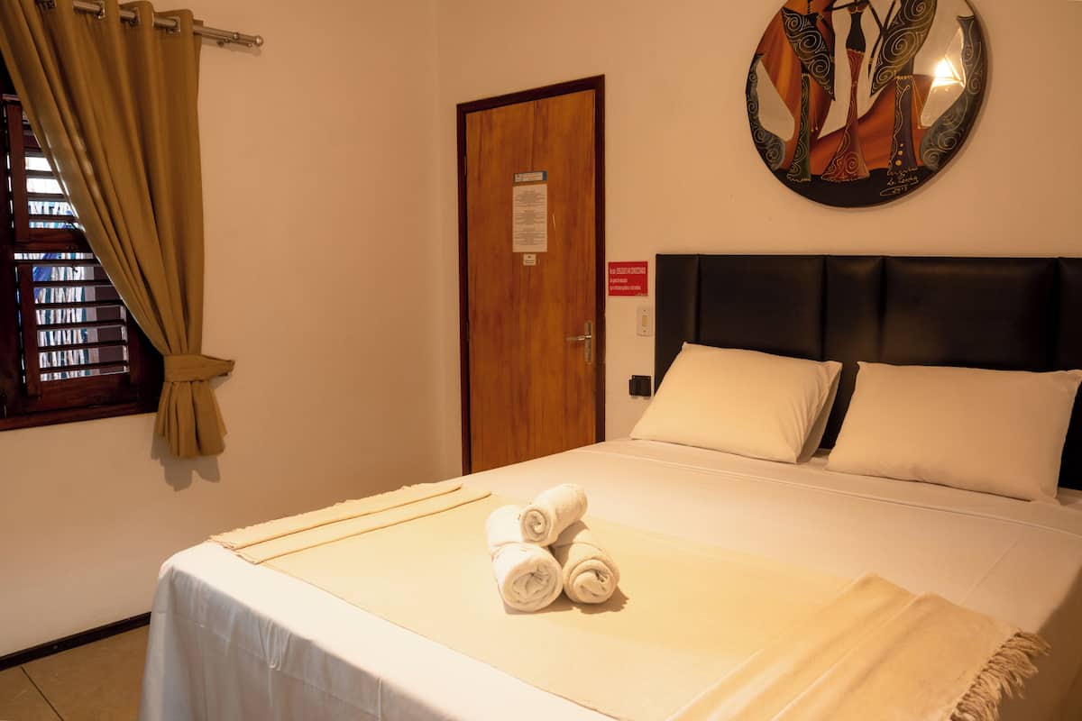 A hotel room with a bed, a door, a window with curtains, and a wall decoration.