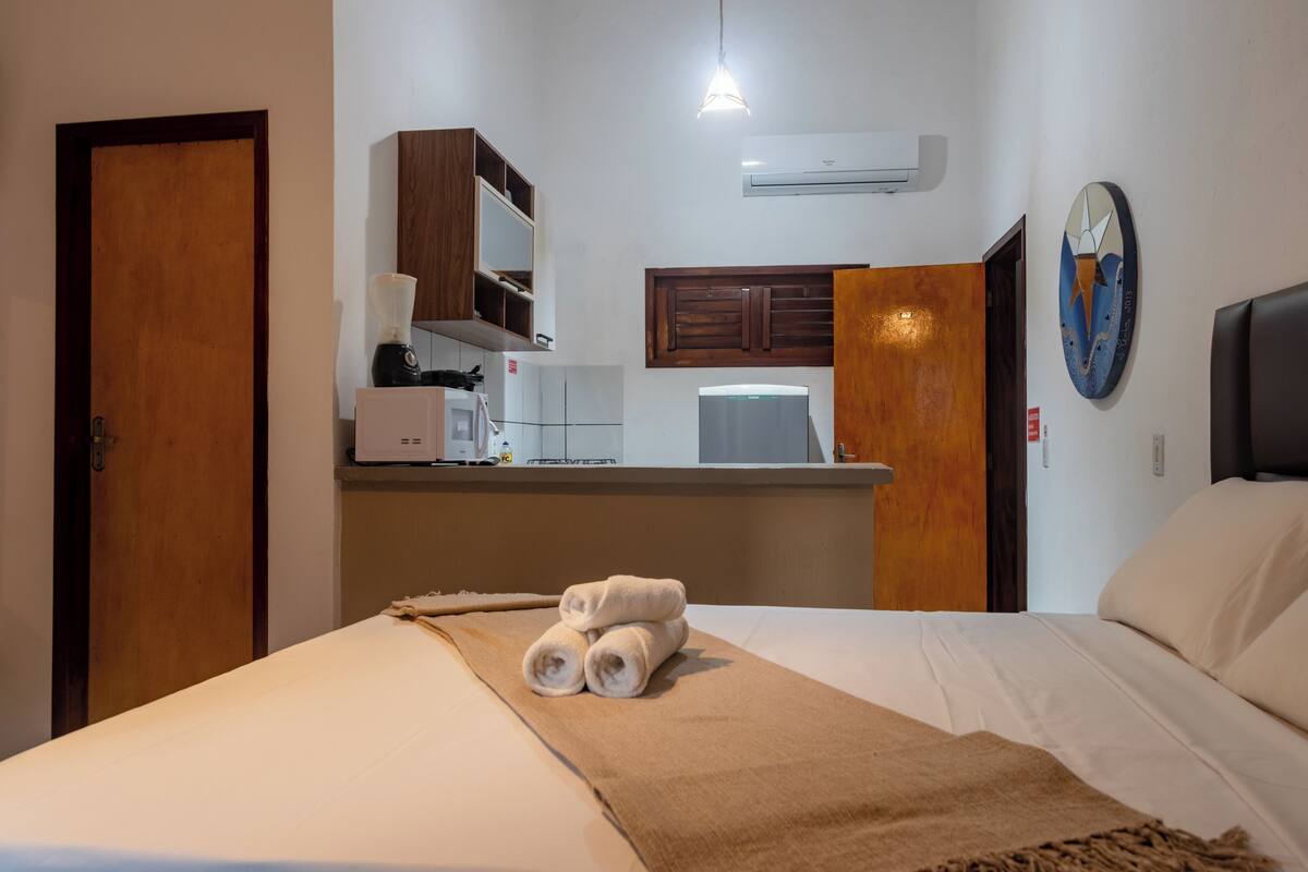 A hotel room with a bed, a small kitchenette, and a bathroom.