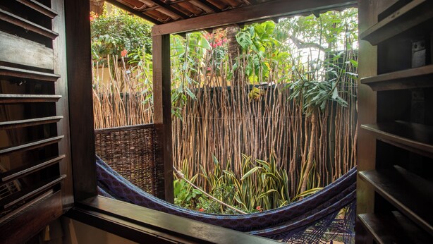 Uma rede em área externa coberta com vista para vegetação exuberante e cerca de bambu.