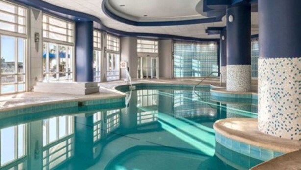 Una grande piscina interna con acqua cristallina e limpida, circondata da ampie finestre e pilastri blu.