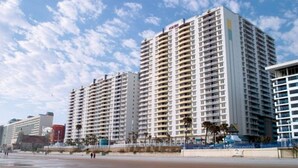 Un hotel di grandi dimensioni con numerosi balconi, situato vicino alla spiaggia.