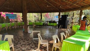 An outdoor covered area with tables and chairs, a tiled floor, and a sign for a company. - Green Hills Resort (Vasai)