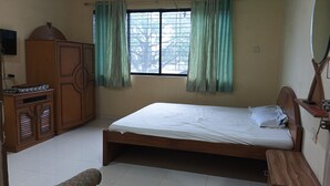 A bedroom with a single bed, wooden wardrobe, and a window with curtains. - Green Hills Resort (Vasai)