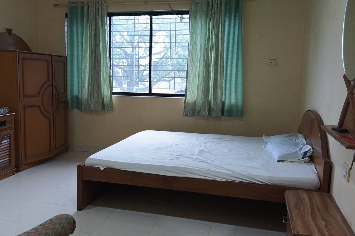 A bedroom with a single bed, wooden wardrobe, and a window with curtains.