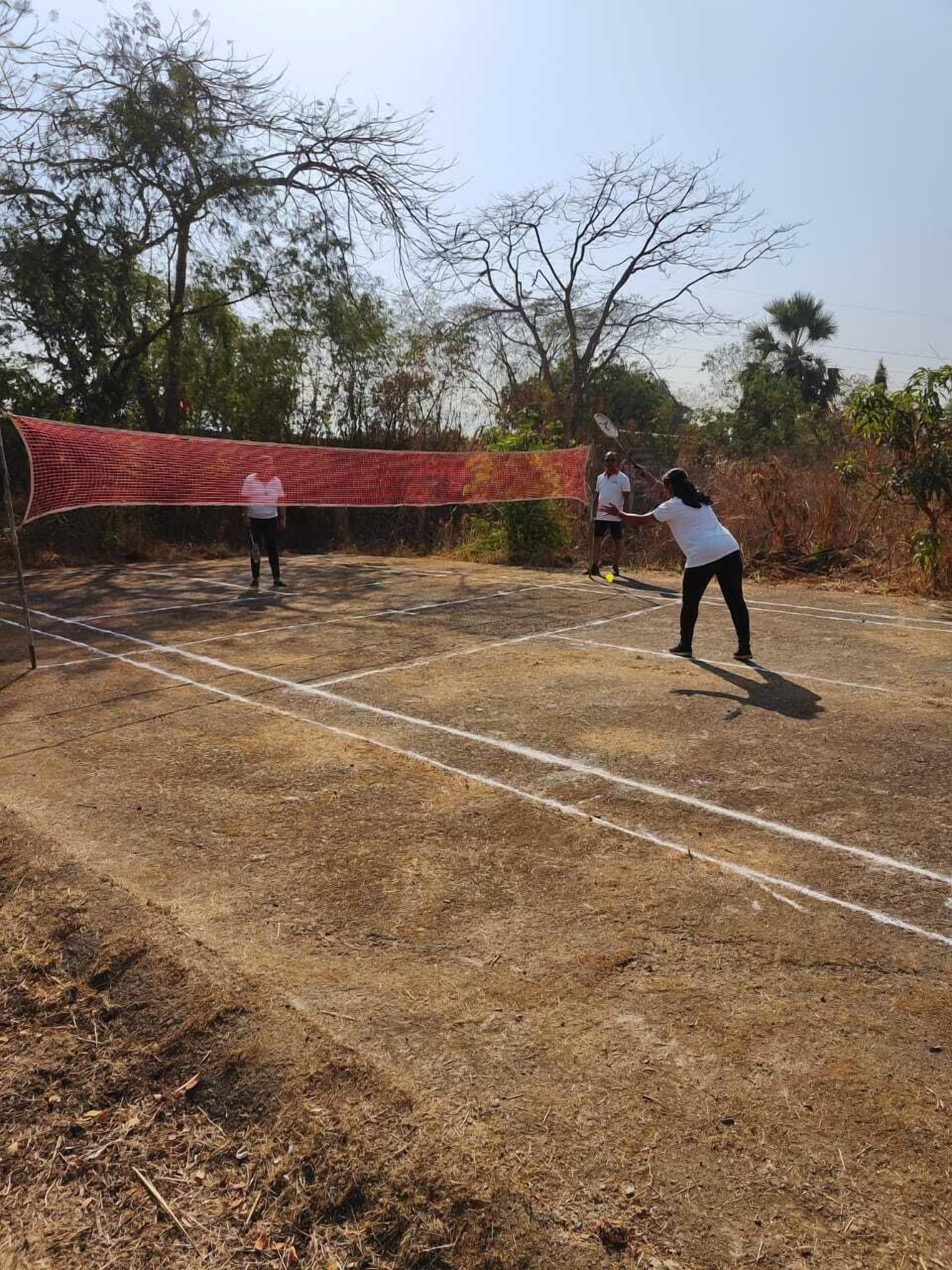 An outdoor tennis court with a net, surrounded by trees and dry grass.