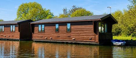 A row of wooden floating houses with windows, a dock, and a small boat.