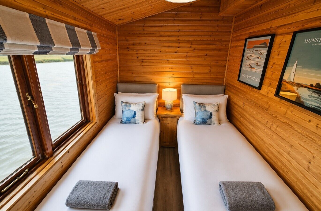 Eine Hütte mit zwei Betten, einem Fenster mit Blick auf das Wasser und einer Lampe auf dem Nachttisch.