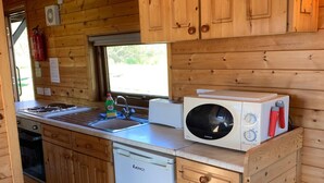 Een kleine keuken met houten kastjes, een vaatwasser, een magnetron en een spoelbak.