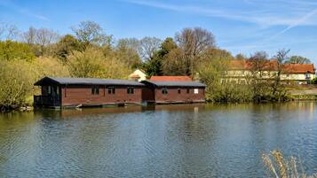 A wooden houseboat with a flat roof and a small deck, floating on calm water.