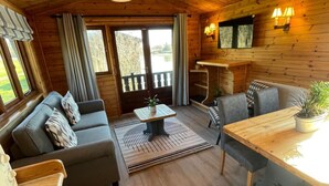 Een gezellig interieur van een blokhut met een bank, eettafel en uitzicht op de natuur door een raam.