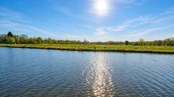 Un río tranquilo que refleja la luz del sol, rodeado de campos verdes y árboles bajo un cielo despejado.