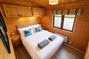 Ein Schlafzimmer einer Holzhütte mit Bett, Kissen, einem Fenster und Blick auf ein Gewässer.