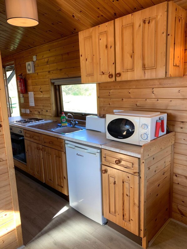 Een kleine keuken met houten kastjes, een vaatwasser, een magnetron en een spoelbak.