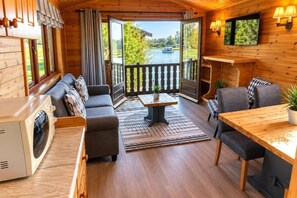 A cabin interior with a sofa, dining table, chairs, a television, and a view of a lake.