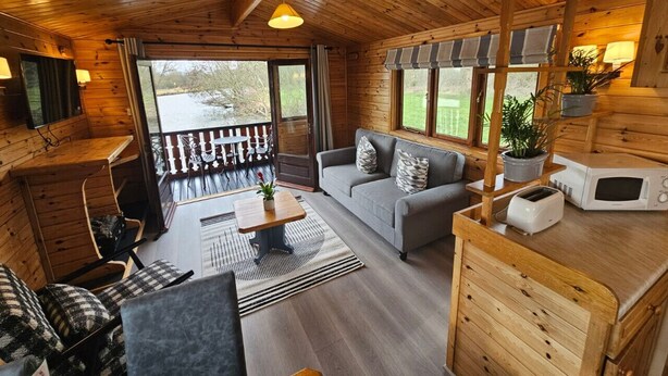 A cozy cabin interior with a wooden ceiling, a sofa, a dining table, and a kitchen area with a microwave.