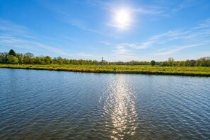 Une rivière paisible reflétant la lumière du soleil, entourée de champs verdoyants et d’arbres sous un ciel dégagé.