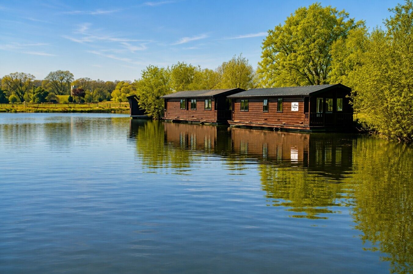 Una cabaña de madera con un muelle que se adentra en un lago tranquilo, rodeada de exuberante vegetación.
