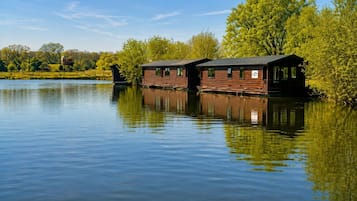 Una cabaña de madera con un muelle que se adentra en un lago tranquilo, rodeada de exuberante vegetación.