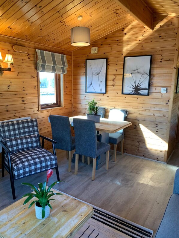 Een gezellig chalet interieur met houten wanden, een eettafel met stoelen, een geruit bankje en twee ingelijste kunstwerken.