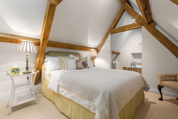 A bedroom with a large bed, wooden beams, a bedside table with a lamp, and a small table with a lamp.