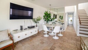 Una cocina moderna con comedor, muebles de cocina blancos y un televisor de pantalla plana grande.